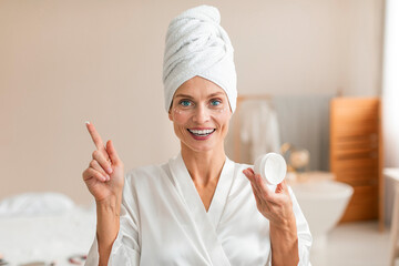 Lovely middle aged woman applying cream under her eyes, making beauty treatment with natural cosmetic product