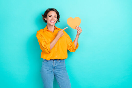 Portrait photo of young attractive pretty woman finger pointing little paper heart smile positive ad isolated on cyan color background
