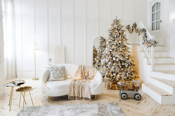 Stylish white living room decorated for Christmas. A room with a white leather sofa and a wooden staircase leading to the second floor. Bright Christmas interior. Holiday. Big Christmas tree. Nobody.