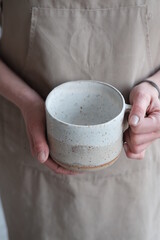 Women in the apron holding handmade clay and turquoise cup of tea. Clay workshop