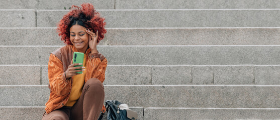 young black woman with mobile phone smiling on street stairs