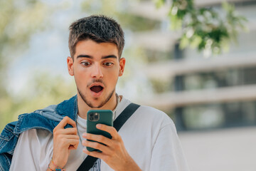 young man in the street looking at the phone with a surprised expression
