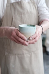 Women in the apron holding handmade clay and turquoise cup of tea. Clay workshop