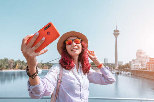 Happy girl travel blogger takes selfie pictures on her smartphone of the famous Dusseldorf TV tower from the Media Harbor canal in the post industrial district. Travel and sightseeing locations