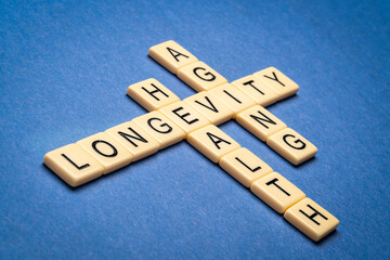 longevity, health and aging crossword word in ivory letter tiles against textured handmade paper,...