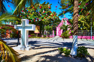 cross and church in the background with blue sky, palm trees and garden, isla aguada campeche 