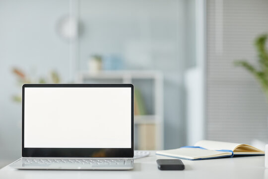 Minimal background image of opened laptop with white screen mockup at workplace in office interior white and grey tones, copy space