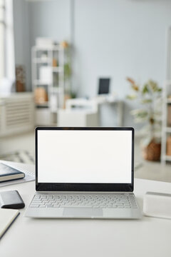 Vertical background image of open laptop with white screen mock up at workplace in minimal office interior white and grey tones
