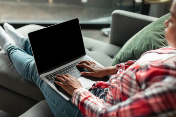 Fototapeta premium Serious millennial african american woman typing on laptop with blank screen on sofa in living room