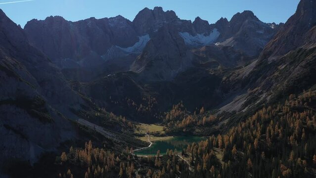 Aerial View Over Seebensee Austrian Alps| Blue Glacial Lake with Tall Mountains and Orange Forest on a Sunny Blue Sky Day