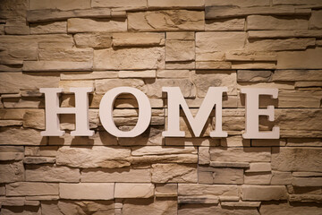 An einer mit schmalen Steinen verkleideten Wand steht das Wort "Home".