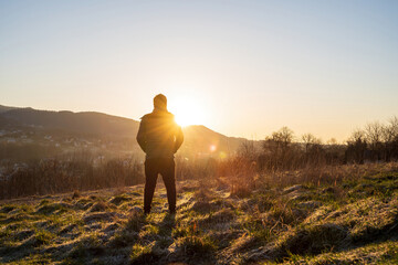 Wide angle shot of a man from behind facing a view of a landscape consists of mountain during sunrise rays in winter.