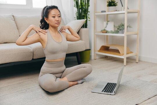 Young Asian woman in front of her laptop sports and yoga repeating exercises on the video at home in lotus position stretching the muscles of the neck, a set of home workouts for the body lifestyle