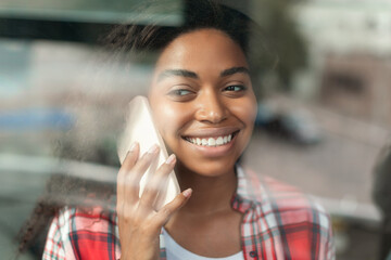 Portrait of cheerful millennial african american woman talking by smartphone, enjoying free time