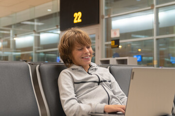 Obraz premium Blond boy waits in an airport lounge while using his laptop computer.