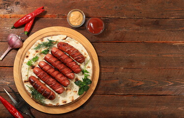 Fried sausages grilled with herbs and seasonings of ketchup and mustard on a wooden background.Top...
