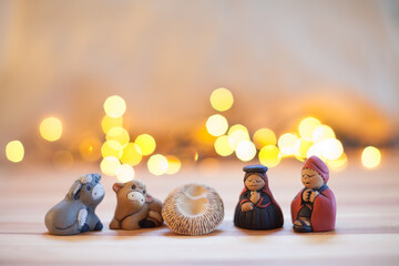 Holy family in colored ceramic and blurred Christmas lights in the background. Christmas decoration.