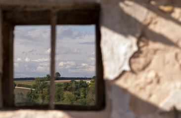 Pola i drzewa , niebo i chmury , widziane , jak obraz w ramie , poprzez okienko starego , zniszczonego  domu .