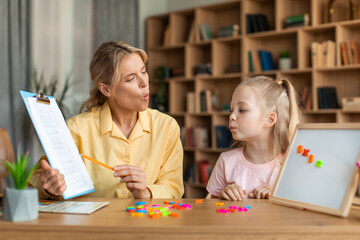 Speech training for kids. Female specialist training with smart little girl, teaching her right articulation exercises