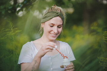 happy alternative & spiritual looking hipster girls makes soap bubbles & blows them in the air outside in the garden with green nature background to have fun 