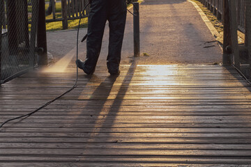 municipal employee cleaning a wooden bridge with a pressure washing machine