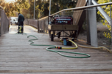 municipal employee cleaning a wooden bridge with a pressure washing machine