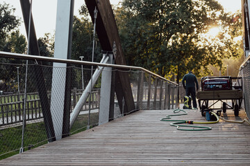 municipal employee cleaning a wooden bridge with a pressure washing machine