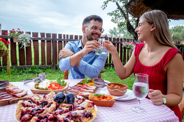 Happy young romantic couple toasting with shots of brandy with a particular narrow neck glasses in a beautiful traditional outdoor country restaurant.