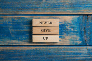 Never give up sign spelled on a stack of three woden pegs