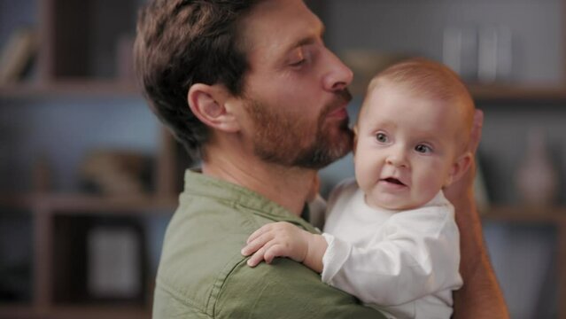 Close-up portrait of a father with a baby in his arms. Dad loves his little daughter, gently kisses. Father is on maternity leave. Paternity Leave. Paternal love