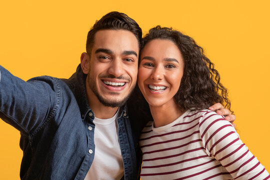 Romantic Cheerful Arab Couple Taking Selfie Together Over Yellow Background,