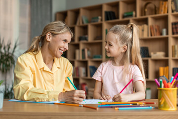 Pretty little girl drawing together with psychologist, kid having therapy session with child development specialist