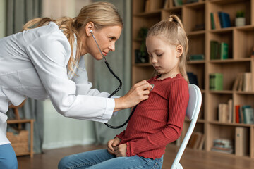 Female pediatrician with stethoscope listening to heartbeat girl's patient on medical exam during...