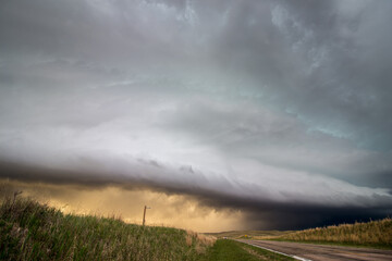 Fototapeta na wymiar A shelf cloud and thunderstorm in the sky over a highway in the grasslands of Nebraska in the evening.