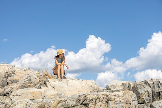 Woman sitting on the rocks in front of the ocean with clouds in the sky