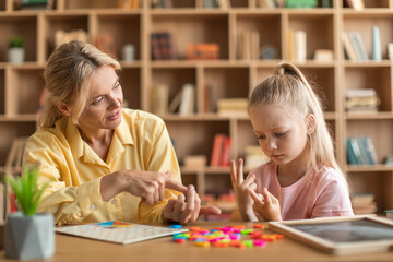 Focused girl preschooler learing to count, sitting with tutor at desk at development classes and studying