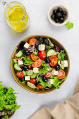 Fresh greek salad with cherry tomato, cucumber, lettuce, black olive, feta cheese and olives oil on gray concrete background.