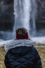Chica de espaldas ante una cascada. Con abrigo negro y cinta del pelo roja.
