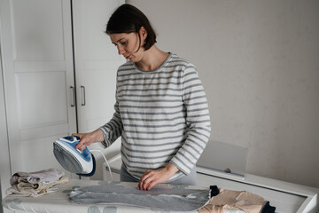 Fototapeta na wymiar Pregnant adult woman ironing newborn baby clothes.