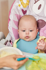 Mom feeds her baby girl with a spoon on baby chair.