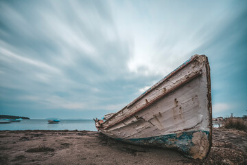 Long exposure photography, abandoned ship on ground and moving clouds at sky as a background