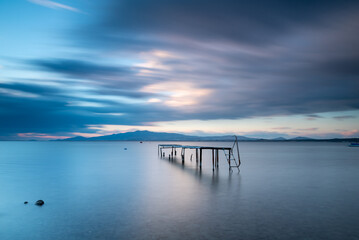 Obraz premium Long exposure photography, wodden pier on foreground and silky sea water and colorful clouds on horizon as a background