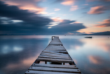 Fototapeta na wymiar Long exposure photography, wodden pier on foreground and silky sea water and colorful clouds on horizon as a background