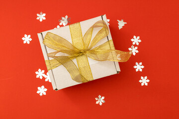 New Year's Eve gift in a white box with a gold golden ribbon on a red background among the sequins