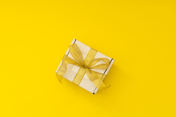 New Year's gift in a white box with a golden ribbon on a yellow background