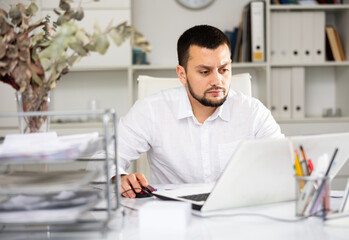 Man office worker sitting at desk and using laptop during his workday.