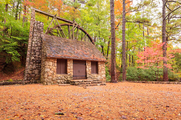 Stone building with chimney and mill wheel in forest during autumn