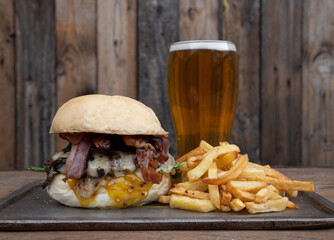 Traditional burger made with bread, bacon, cheddar cheese, lettuce and tomato, french fries and a...