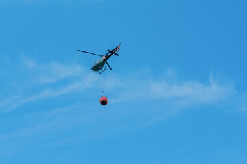 Fototapeta na wymiar Annecy, france - september 2022: Distant helicopter carrying sack of water to pour on a fire.