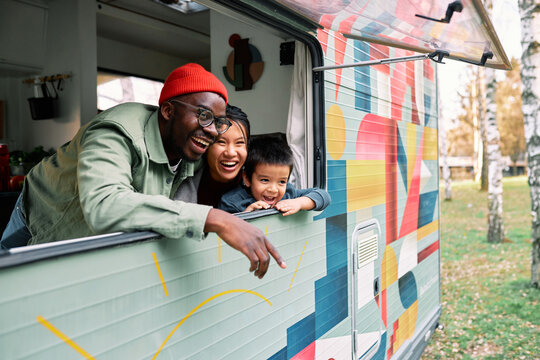 A happy multicultural family sits in their van and looks through the window.